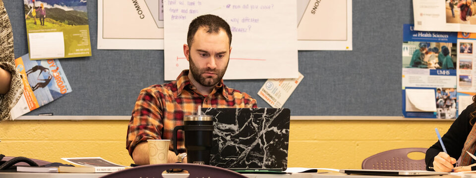 Young man sitting at meeting table looking at laptop.