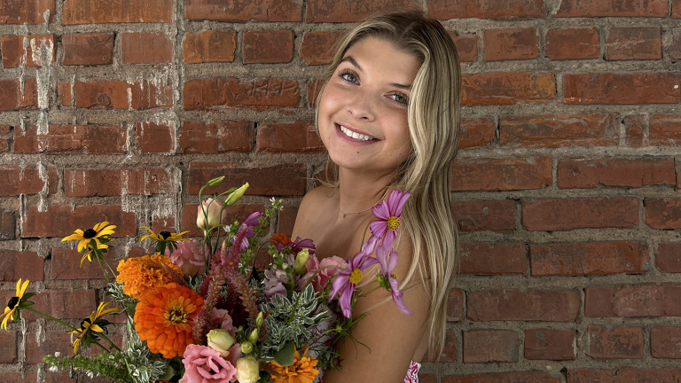 Kelsey Wathen holds a bouquet of flowers for a photo in front of a brick wall