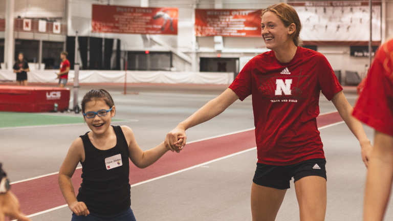 Jenna Rogers smiles while holding hands with a smiling young girl at the Everybody Plays Mini Camp (Husker Athletics)